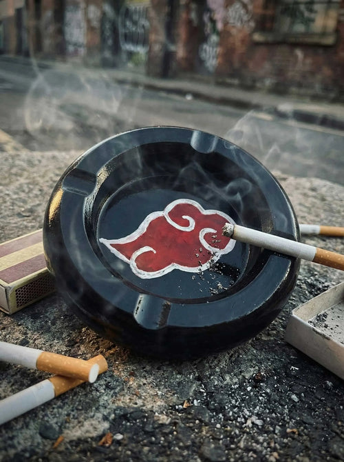 Black  concrete ashtray with red cloud symbol of Akatsuki containing a lit cigarette on a street background