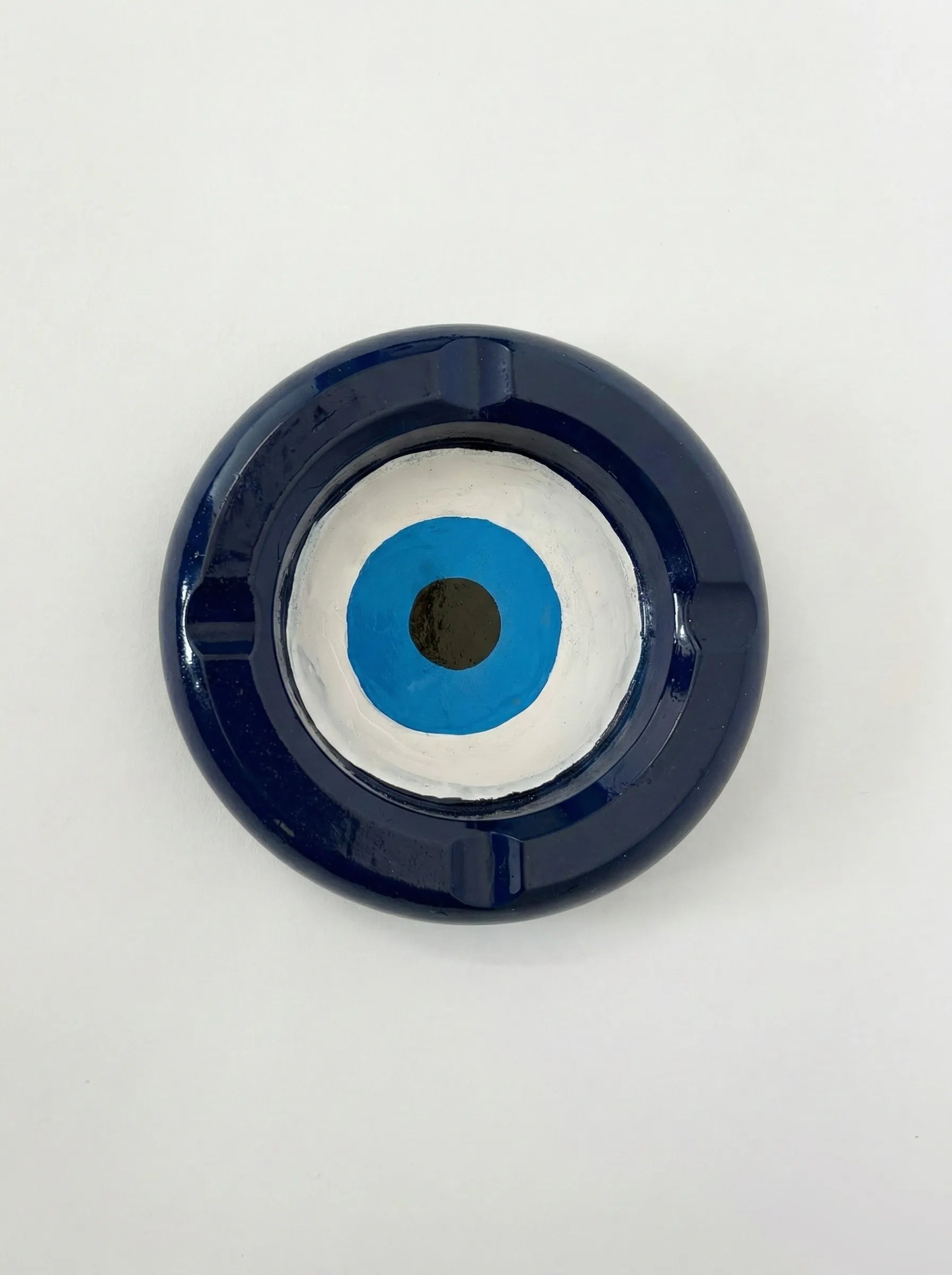 Round blue and white ashtray with a central black dot on a light gray background