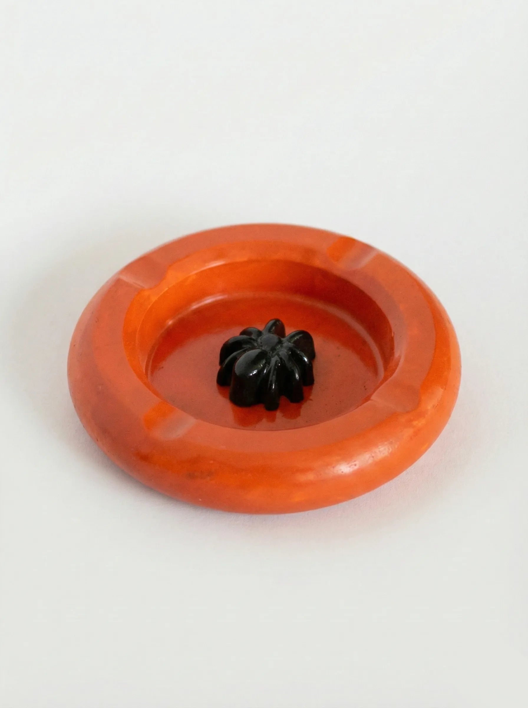 Orange ashtray with a black spider on a white background