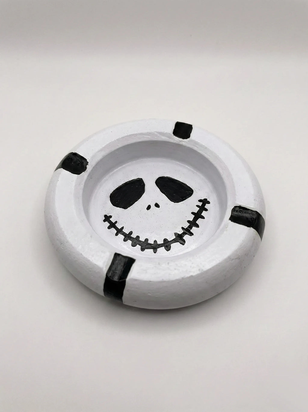 Round white ashtray with mime face design on a light gray background