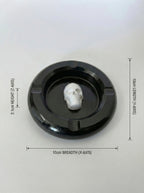 Black circular ashtray with a white skull-like figure inside, on a light gray background with measurements indicated.