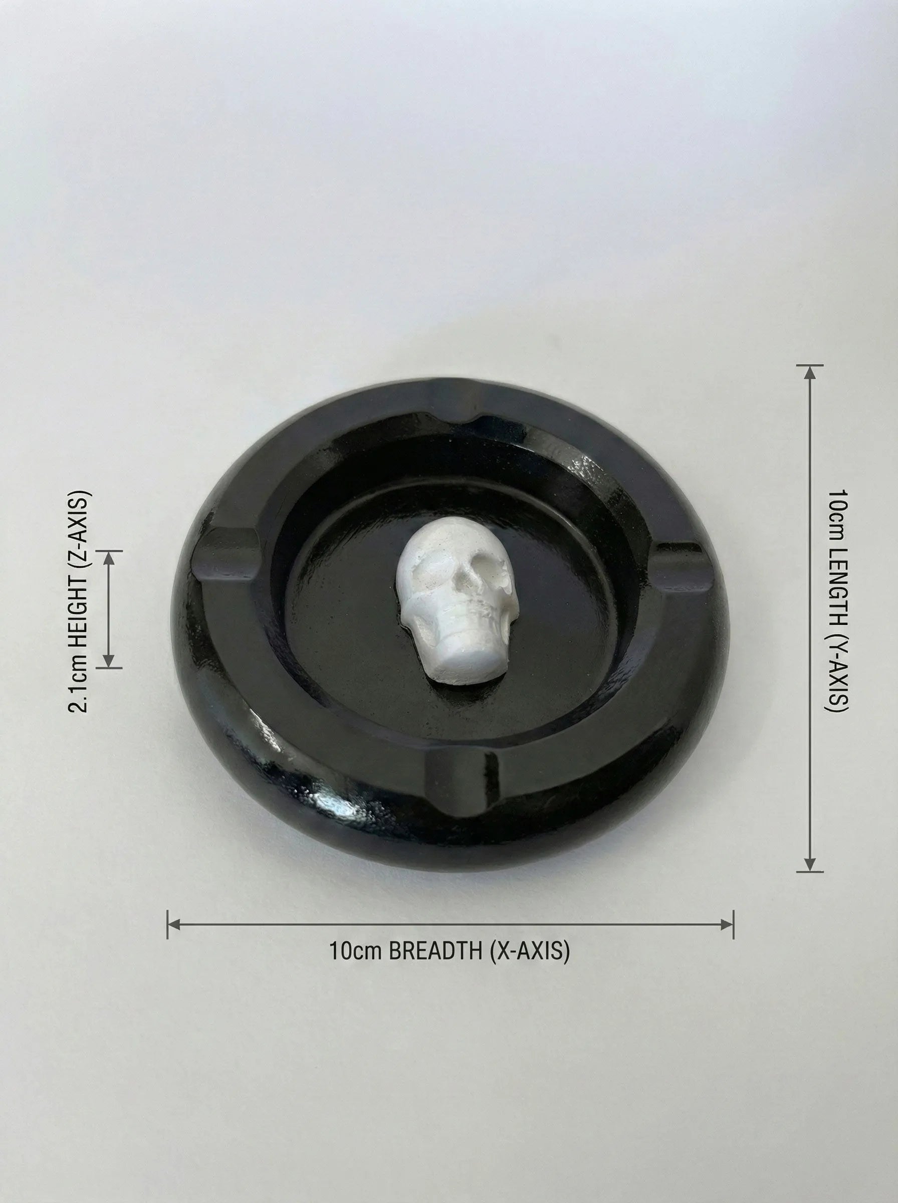 Black circular ashtray with a white skull-like figure inside, on a light gray background with measurements indicated.