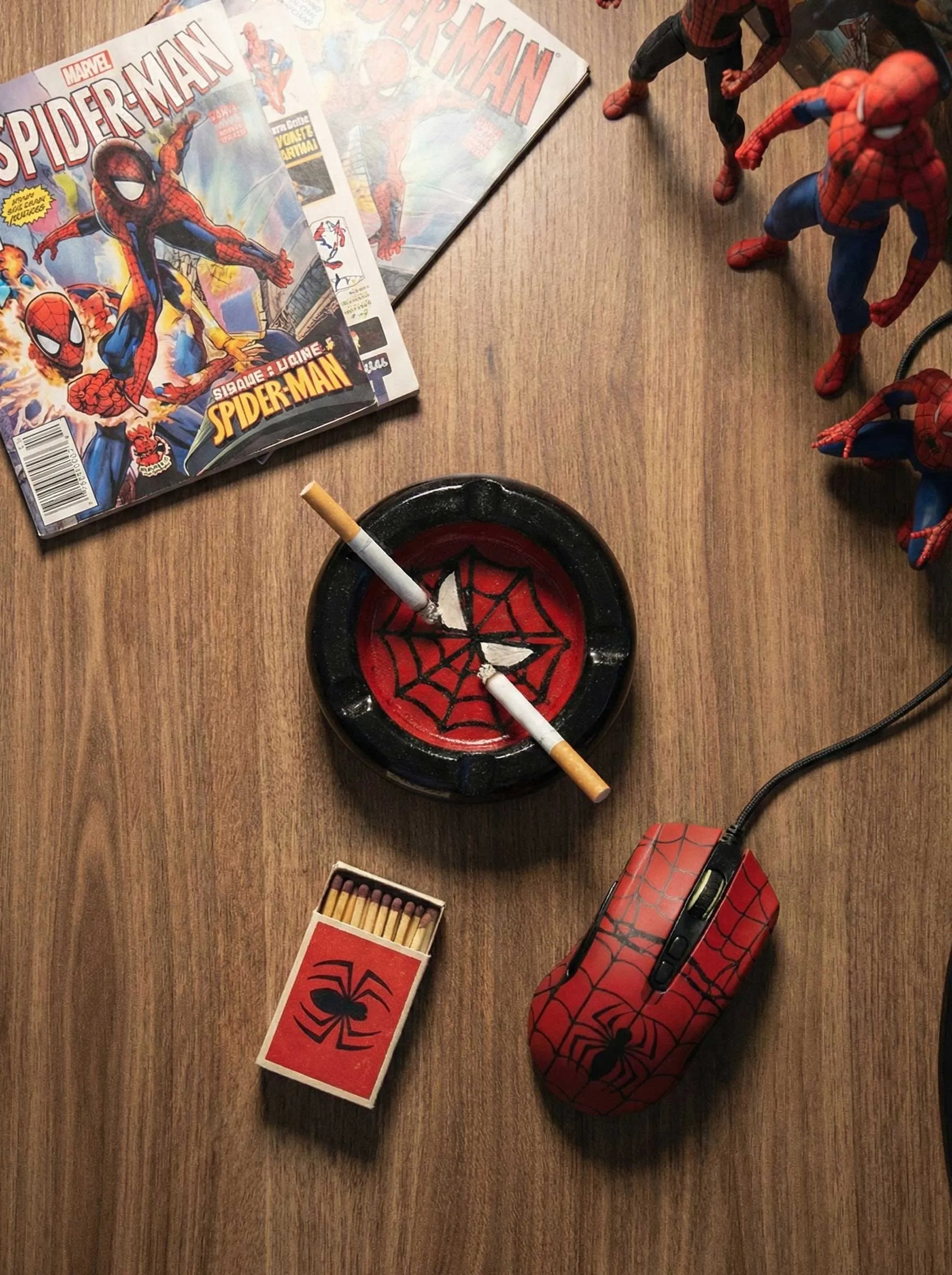 Spider-Man themed items including comic books, figurines, an ashtray, and a mouse pad on a wooden surface.