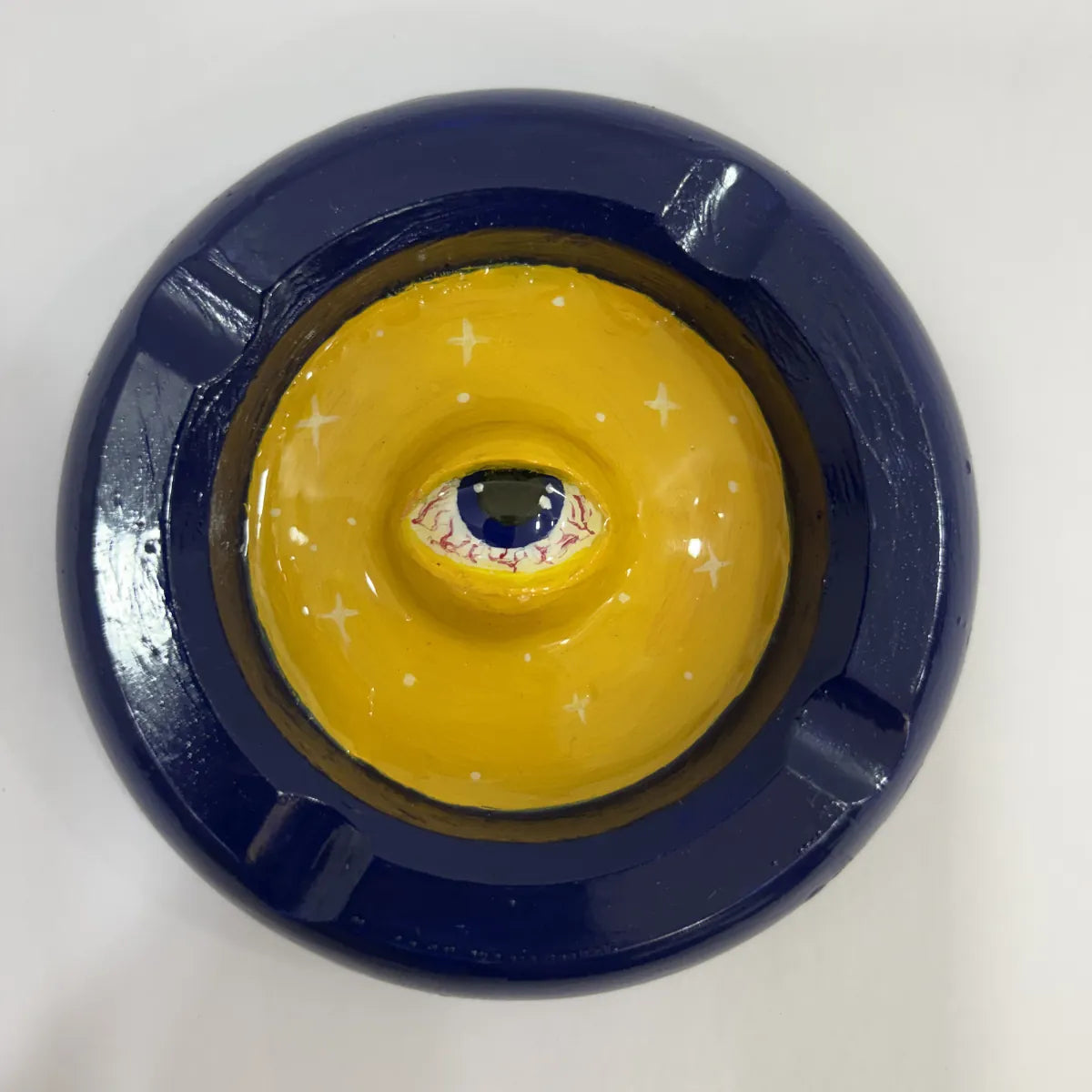 Top view of a blue and yellow ashtray with a central eye design on a white background