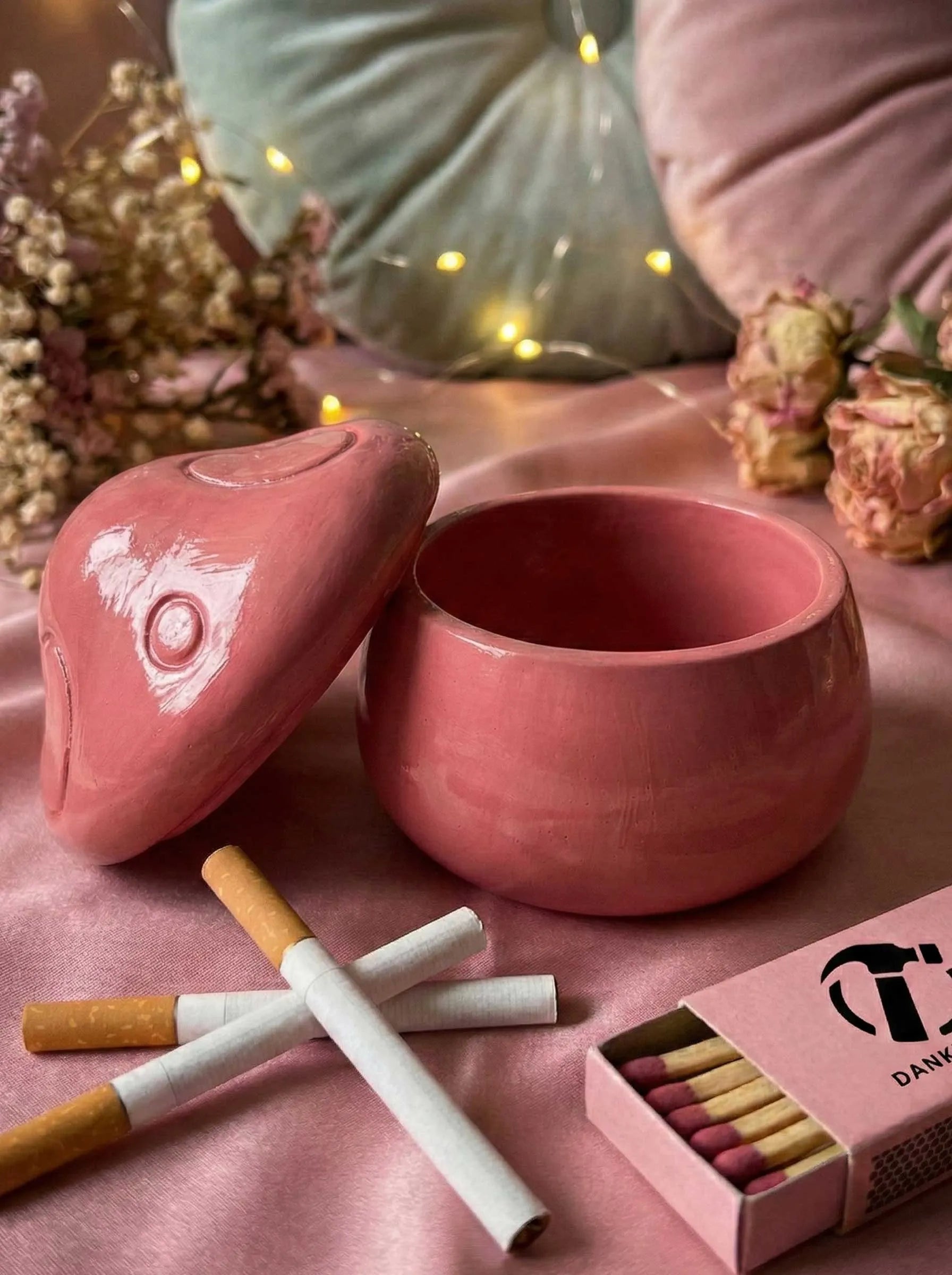 Pink ashtray with Lid, cigarettes and matches on a pink surface