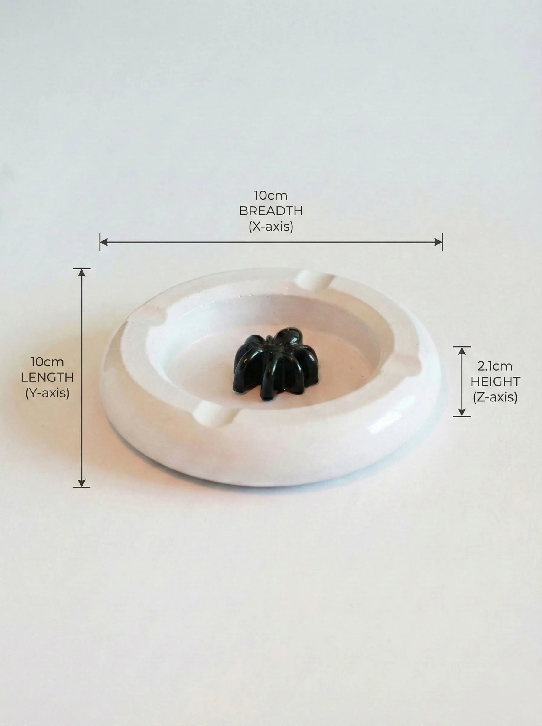 White circular ashtray with black spider-like figure, shown with measurements on a white background